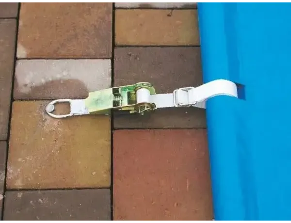 Grün-weißes Spannseil mit Ratsche sichert eine blaue Poolabdeckung mit Handbedieneinheit